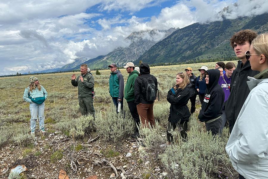 Tyler Brasington stands with students amidst mountains, fields, and puffy clouds.