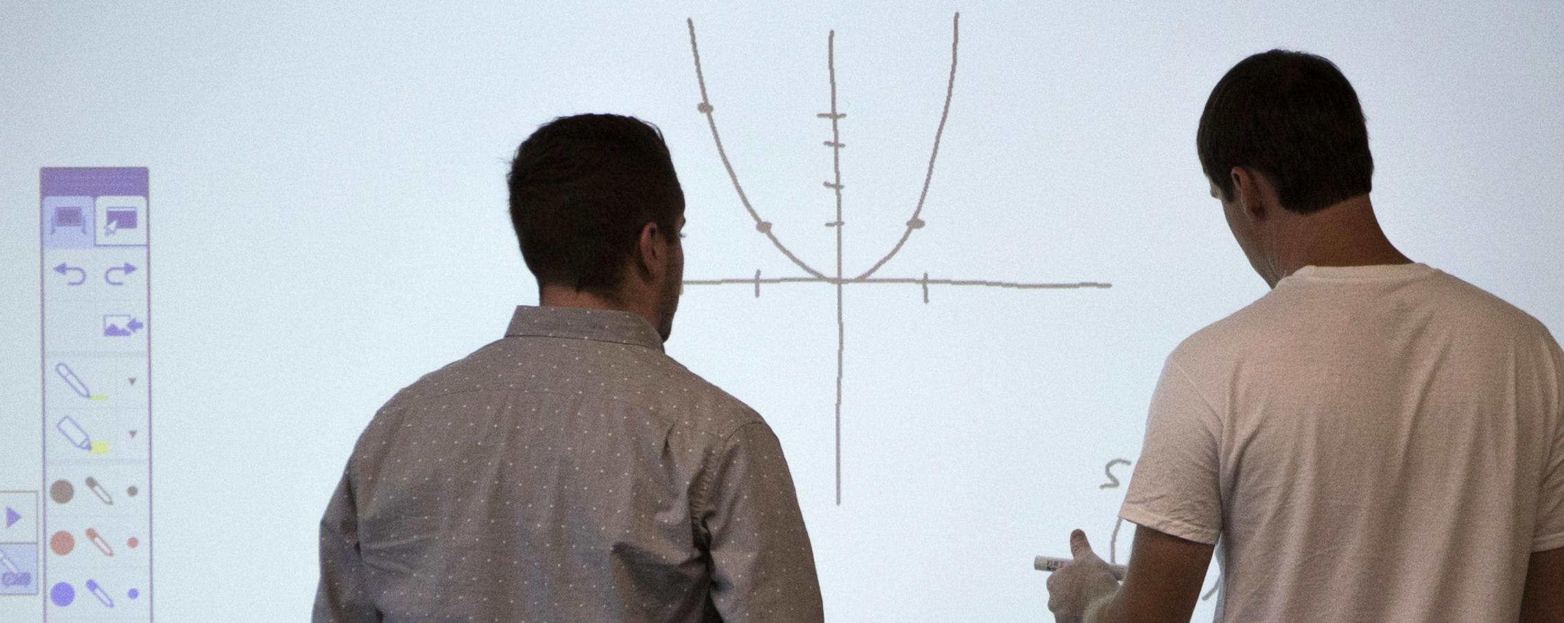 Two people work together at a white board, looking at a graph.