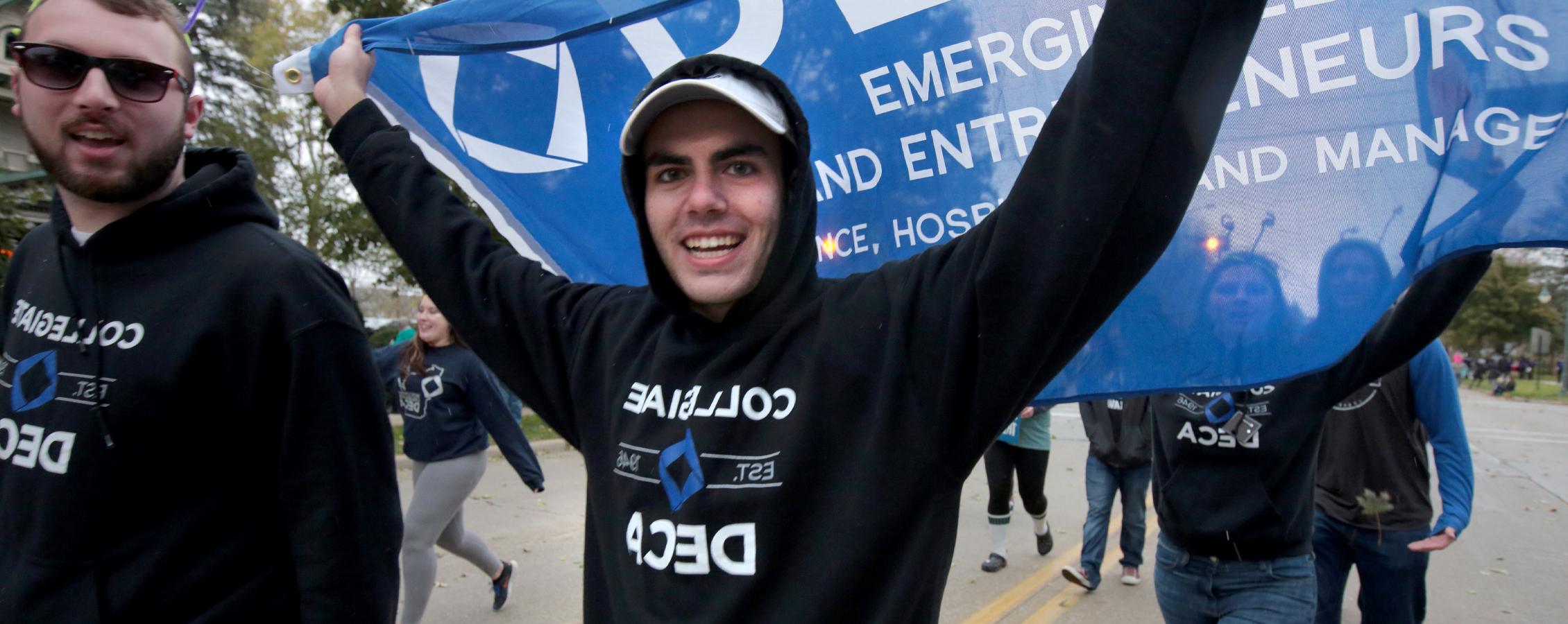 A student wears a DECA shirt and waves a DECA flag.