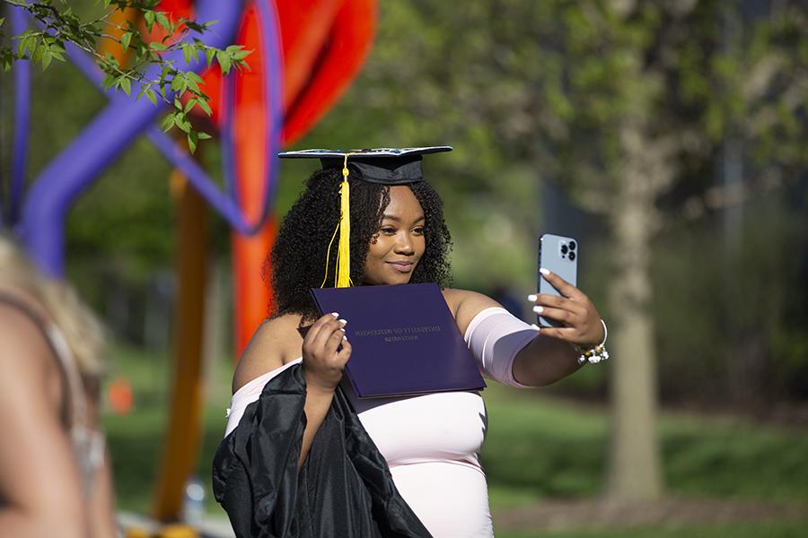 A student in a graduation cap takes a selfie.