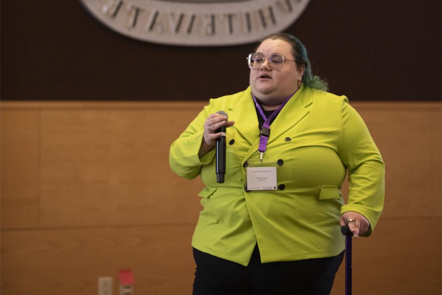 A person in a yellow coat speaks into a microphone.