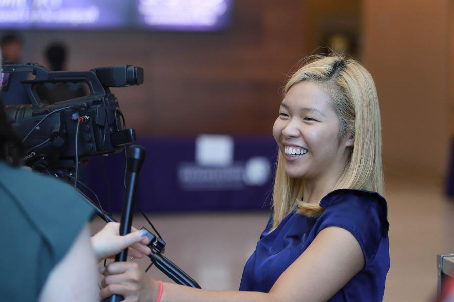 A student stands next to a video camera, smiling.