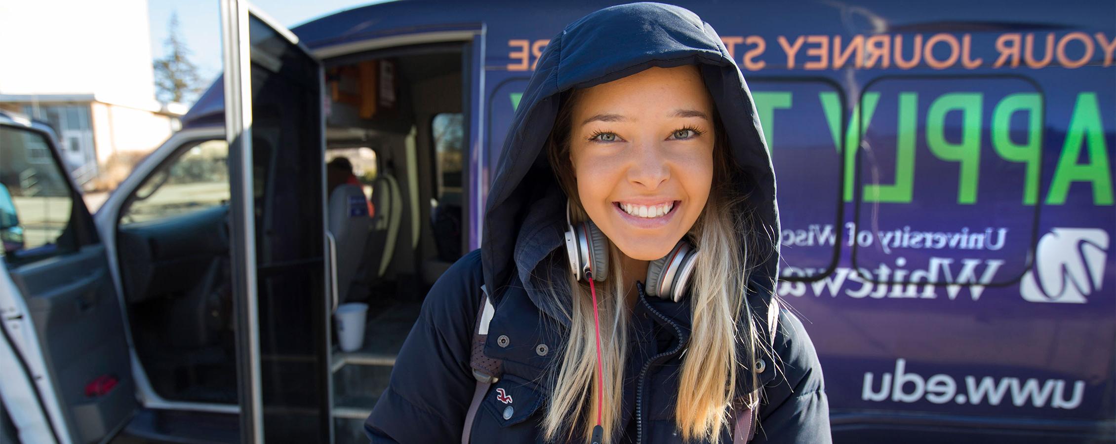 A student smiles at the camera as she stands in front of a purple Warhawk shuttle.