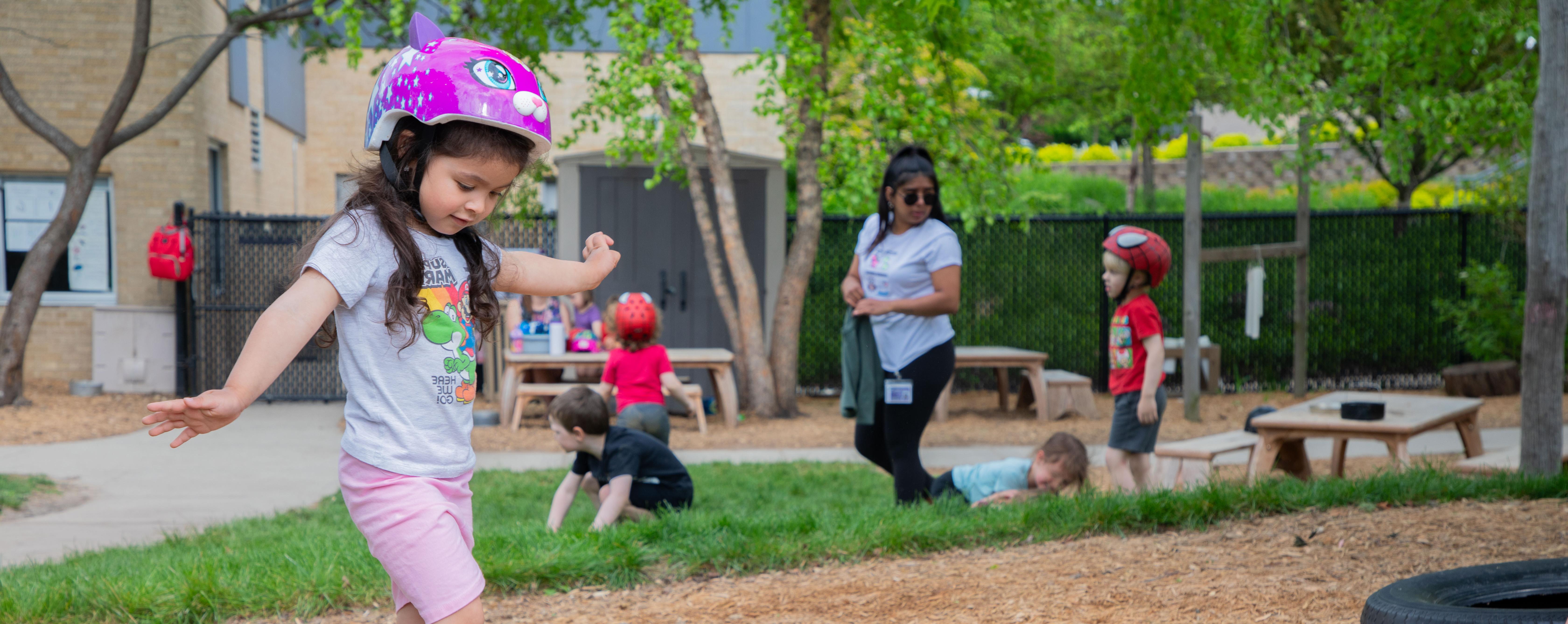 Image of a girl wearing a pink bicycle helmet with other children playing in the background