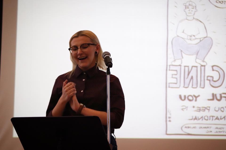 Student stands in front of a microphone to deliver a welcome to invited writer Ivan Coyote. 