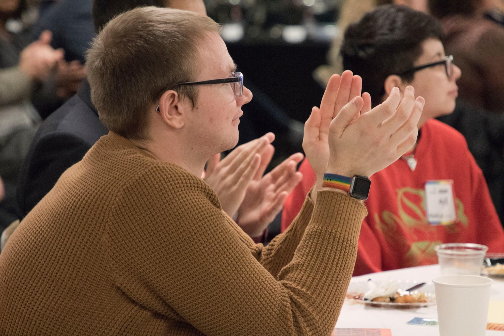 Two student sitting at a table watching a speaker. One is clapping. 