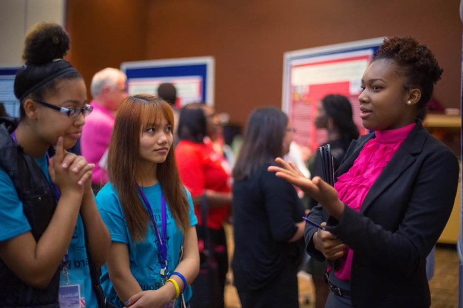 Three students talk with research posters in the background.