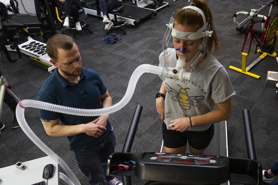 A student runs on the treadmill with a tube connecting from her face to a computer.