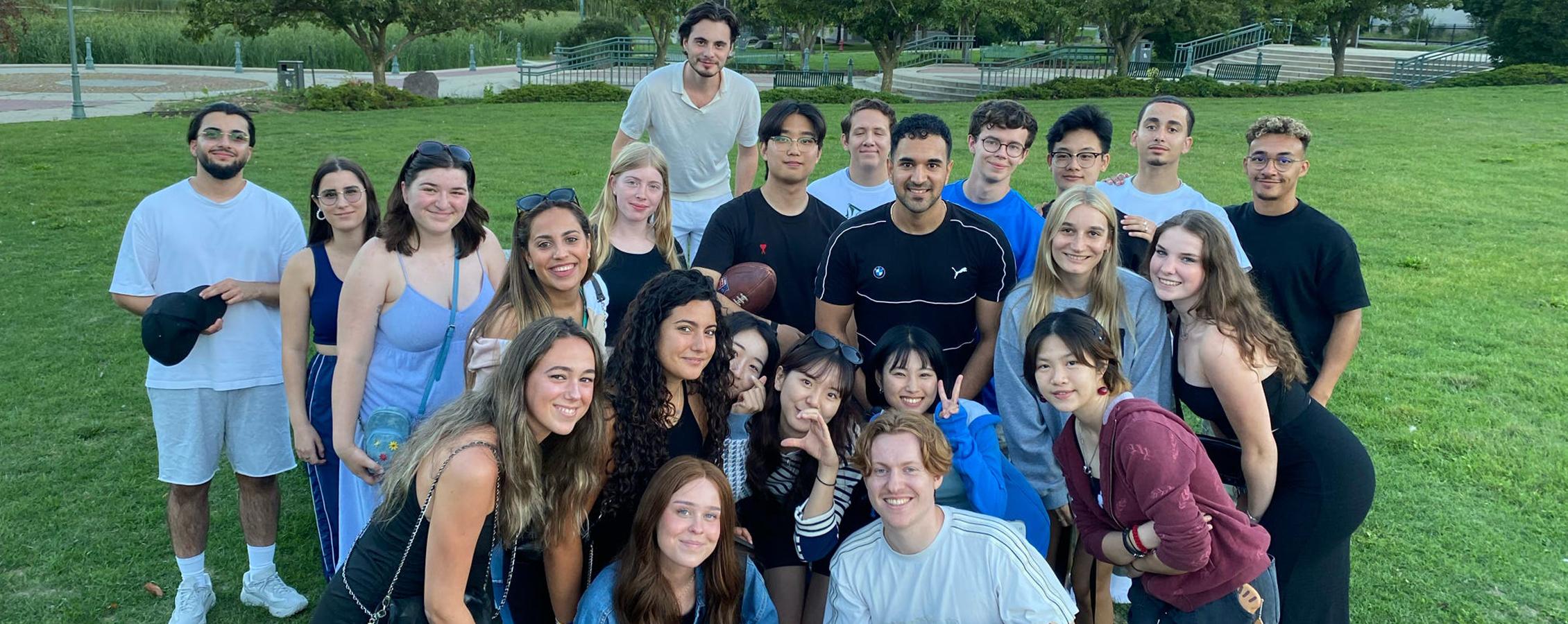 A group of international students celebrate with a red, white, and blue cake in a park.