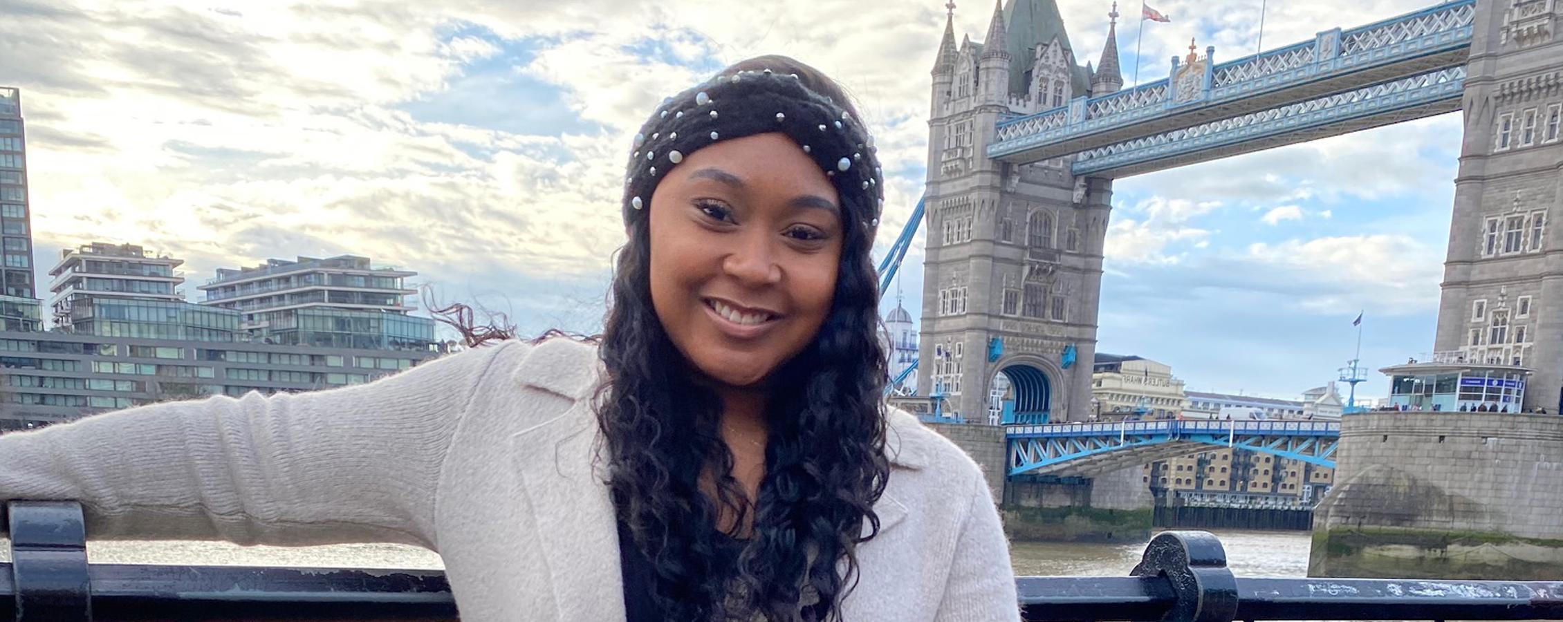 A person poses for a picture by a large bridge in London.