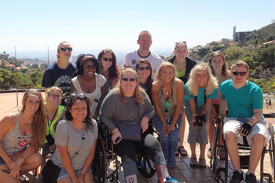 A group of people smile at the camera with mountains and clouds behind them.