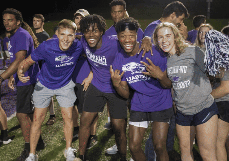 A group of students in purple shirts cheer for the camera.