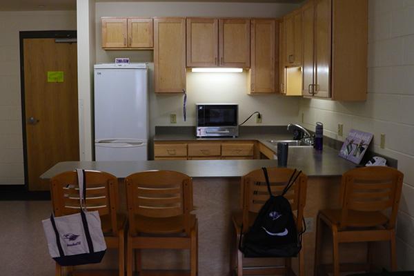 A kitchen with many cabinets, a fridge, a combined toaster oven and microwave, and a breakfast bar.