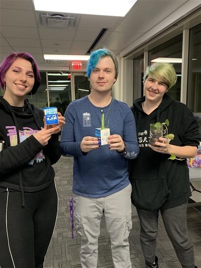 Three students holding plants potted in milk cartons and water bottles