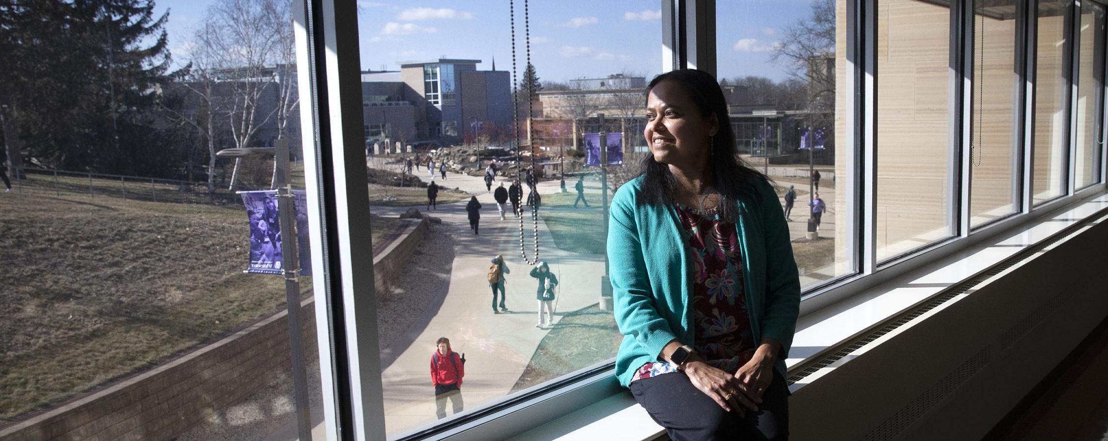 Rashiqa Kamal sits indoors on a windowsill and looks outside.