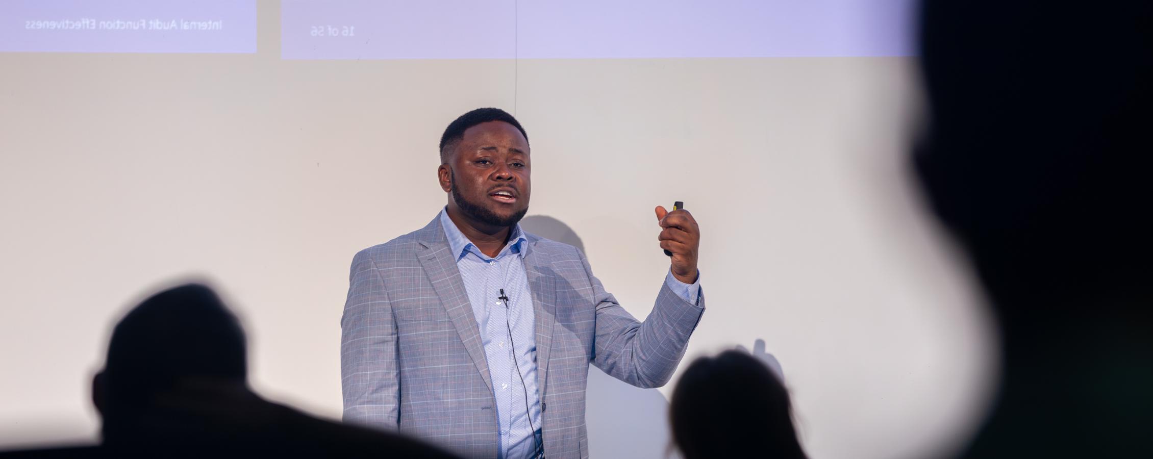 A graduate student from Africa speaks at the front of a lecture hall.