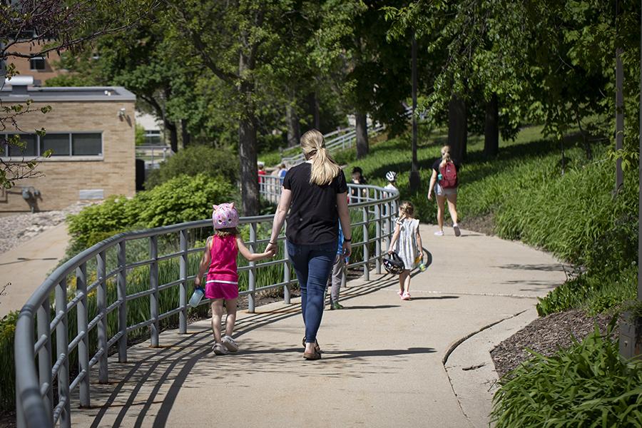 A teacher from the Children's Center holds hands with a child as they walk down a path on campus.