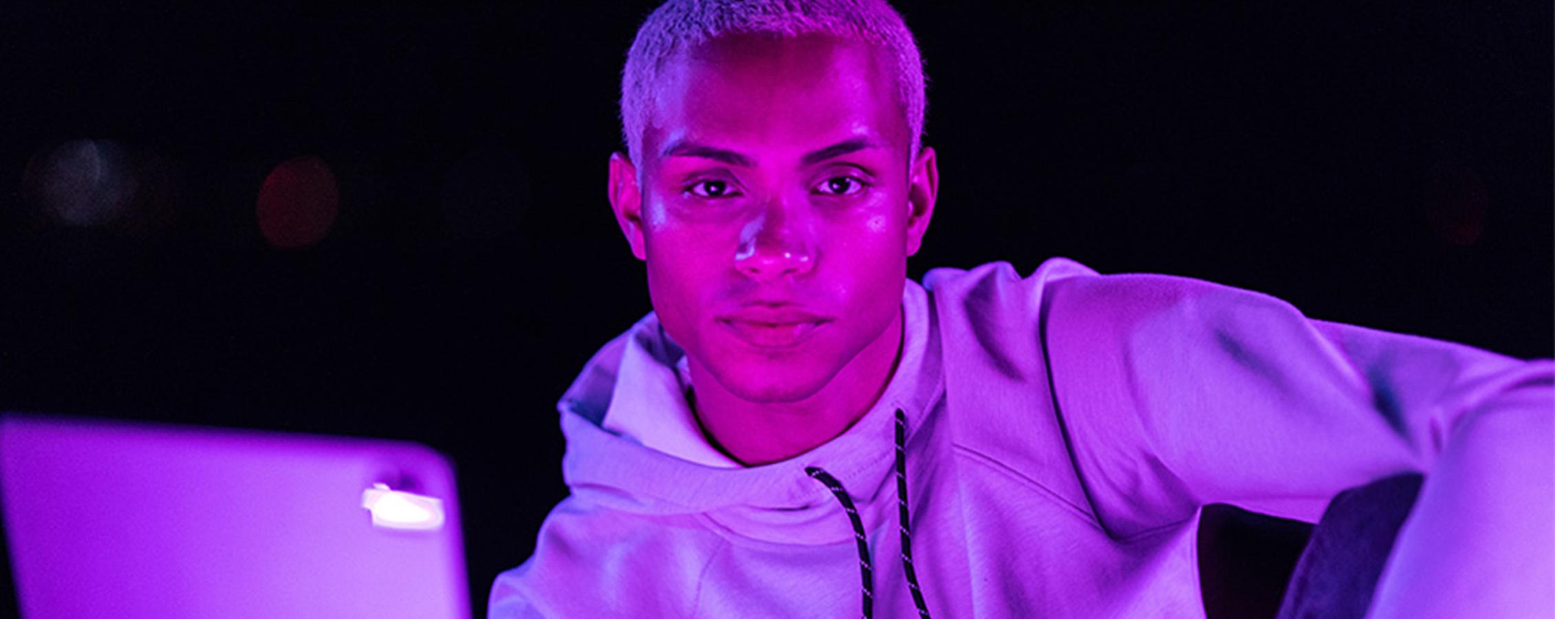 Young man reading tablet in purple light for online  college class